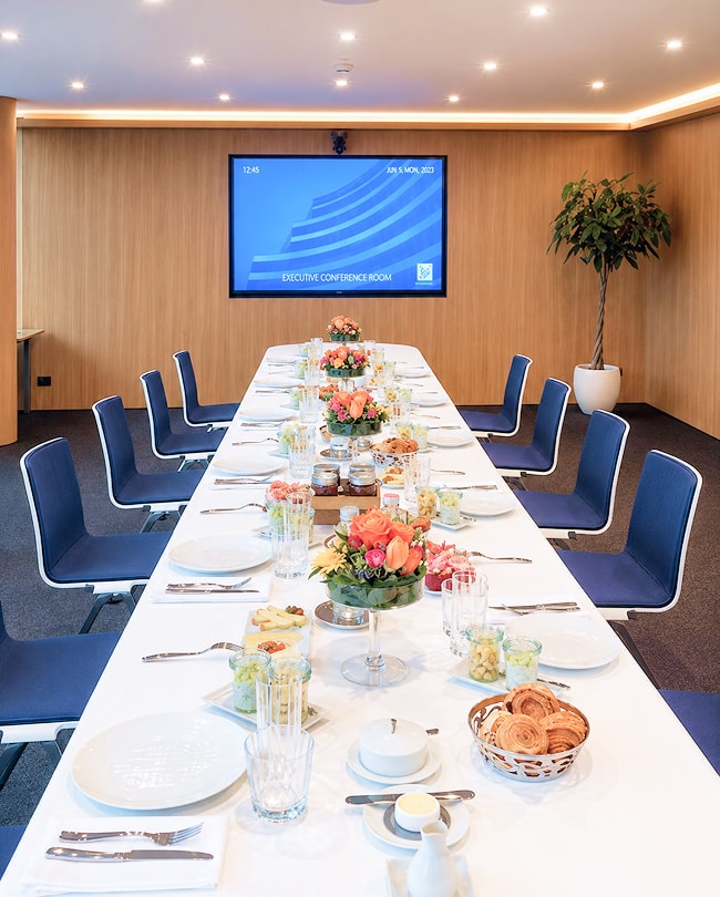 Salle de réunion dressée pour un déjeuner de travail, longue table fleurie