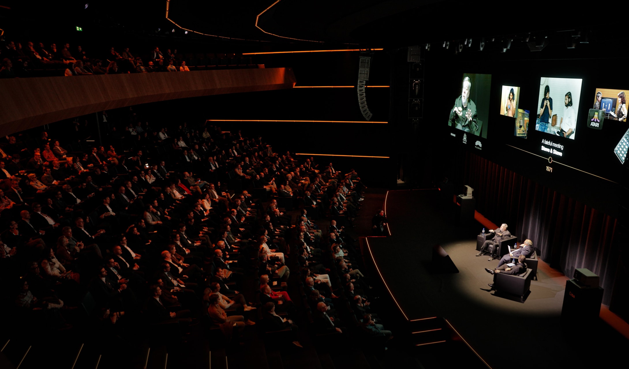 Panel discussion before a packed audience in The Stage, speakers on screen