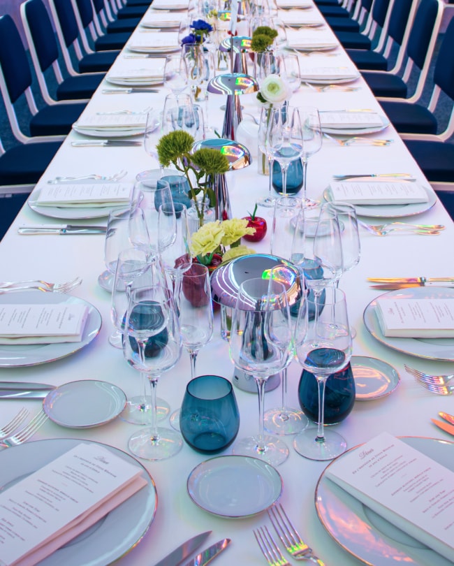 Longue table de banquet dressée avec verrerie, fleurs et menus