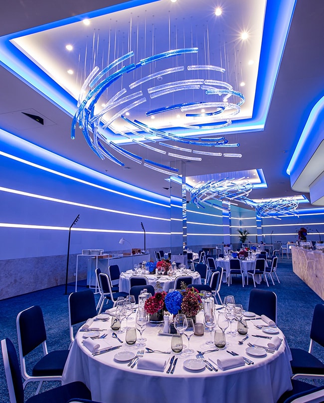 The Space in banquet layout, round tables beneath blue light sculptures